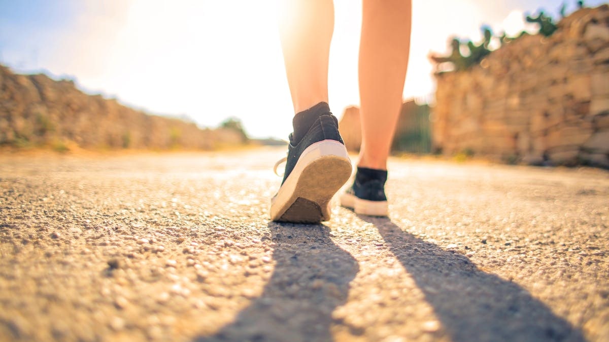 A woman walks down a sunlit path in summer, highlighting leisure and travel outdoors.