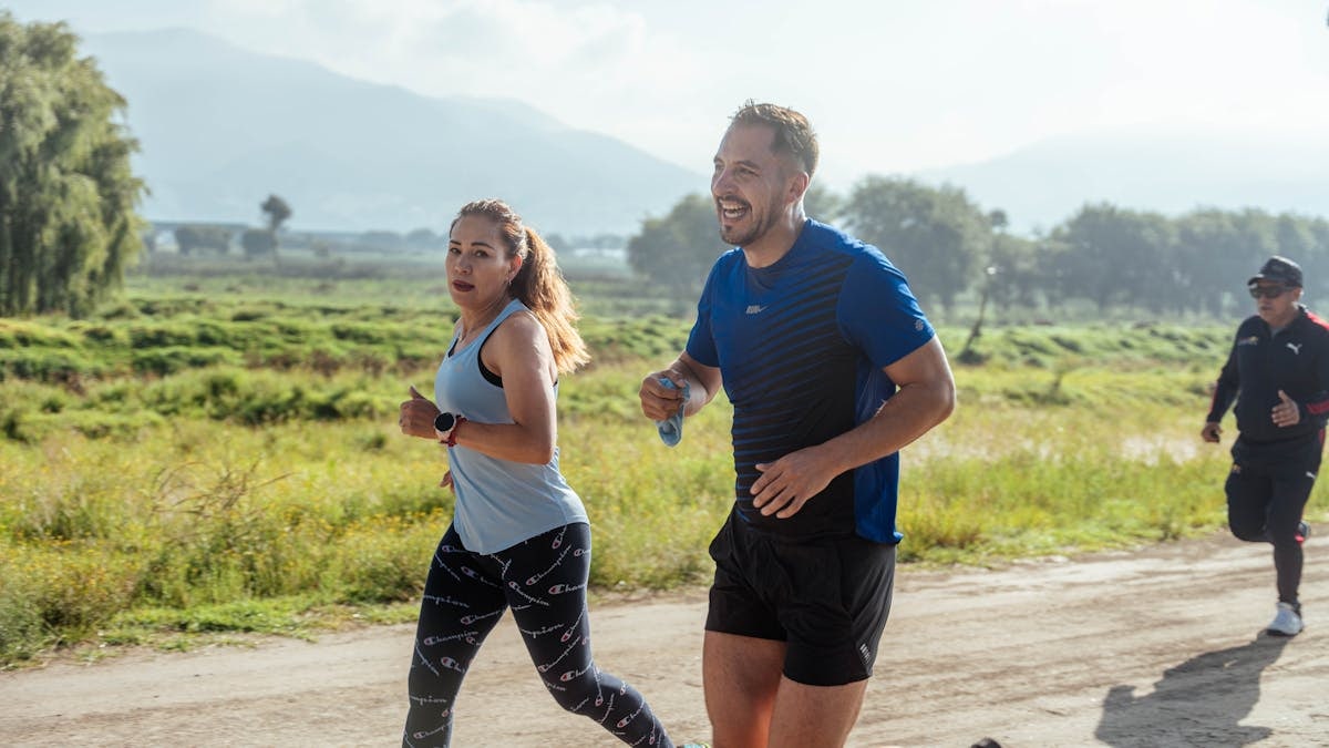 Two adults running on a rural dirt path, enjoying a sunny day outdoors.